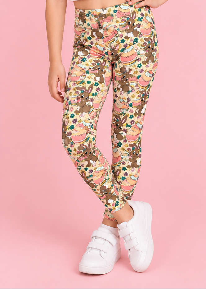 A young girl modeling patterned leggings with a white crop top and white sneakers against a solid pink background. The image includes two inset views: a close-up of the side pocket holding a phone, and a back view of the model wearing the leggings.